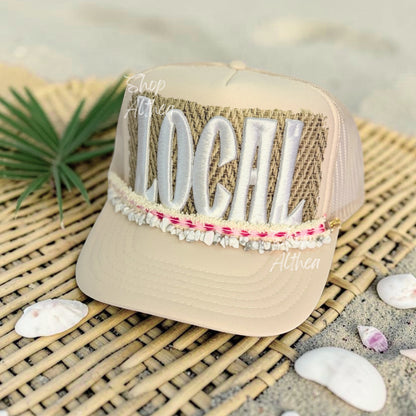 Shop Althea Designs & Patches cream trucker hat with textured woven patch and white embroidered "LOCAL" lettering. Features shell-inspired hat chain.